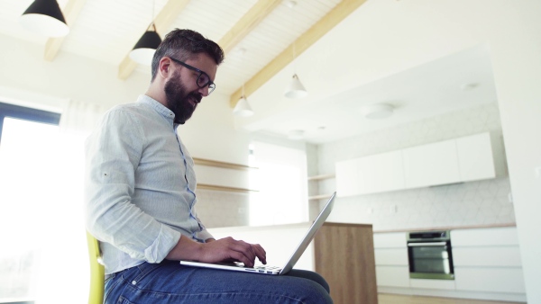 A mature man sitting on chair in unfurnished new house, using laptop. A new home concept.