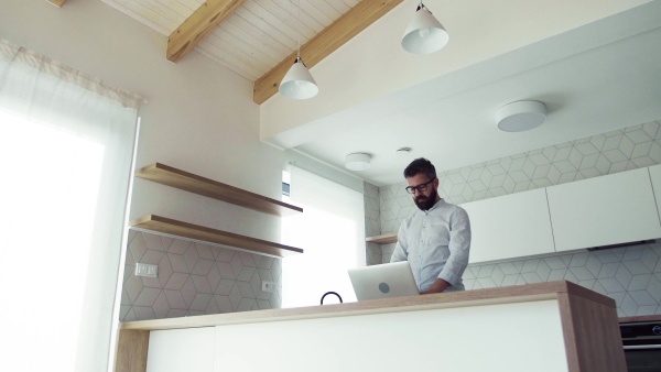 A mature man with laptop standing in kitchen in unfurnished new house. A new home concept.