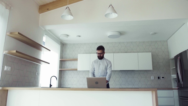 A mature man with laptop standing in kitchen in unfurnished new house. A new home concept.