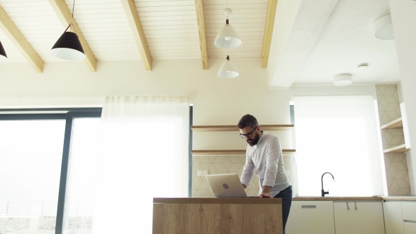 A mature man with laptop standing in kitchen in unfurnished new house. A new home concept.