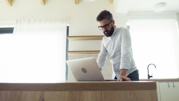 A mature man with laptop standing in kitchen in unfurnished new house. A new home concept.