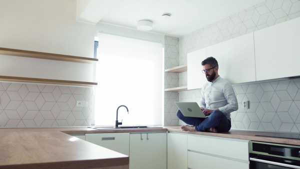 A mature man with laptop standing in kitchen in unfurnished new house. A new home concept.