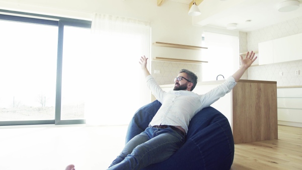 Cheerful mature man sitting on bean bag in unfurnished house, moving in new home concept.