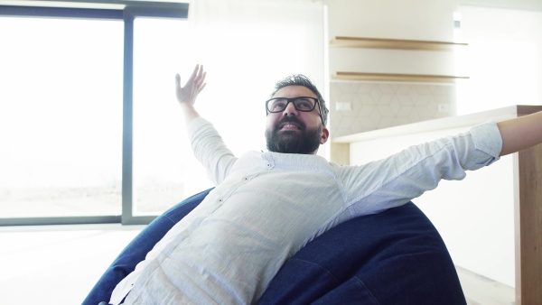 Cheerful mature man sitting on bean bag in unfurnished house, moving in new home concept.