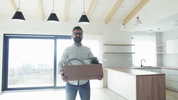 A mature man standing in unfurnished house, holding a box. A moving in new home concept.