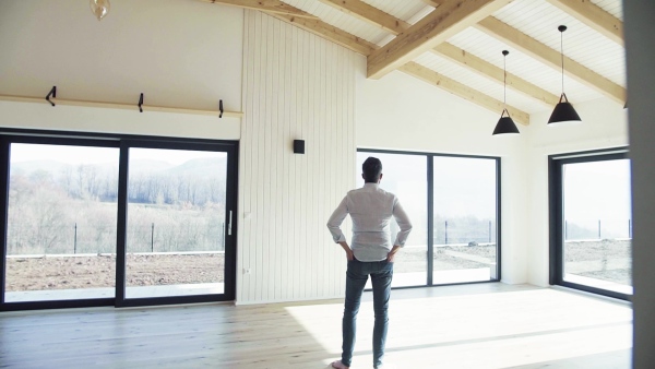 Rear view of mature man standing in unfurnished house, moving in new home concept. Slow motion.