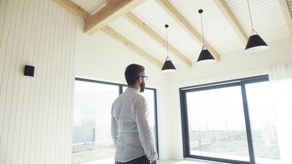 A mature man looking around unfurnished house, moving in new home concept. Slow motion.