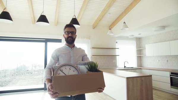 A mature man standing in unfurnished house, holding a box. A moving in new home concept. Slow motion.