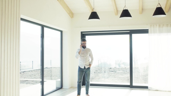 Mature man with smartphone in unfurnished house, moving in new home concept. Slow motion.