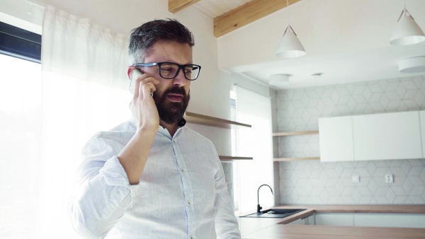 Mature man with smartphone in unfurnished house, moving in new home concept. Slow motion.