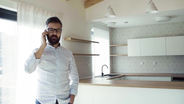 Mature man with smartphone in unfurnished house, moving in new home concept. Slow motion.