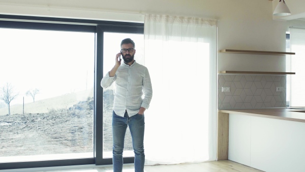 Serious mature man with smartphone in unfurnished house, moving in new home concept.