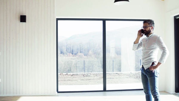 Mature man with smartphone in unfurnished house, moving in new home concept. Slow motion.