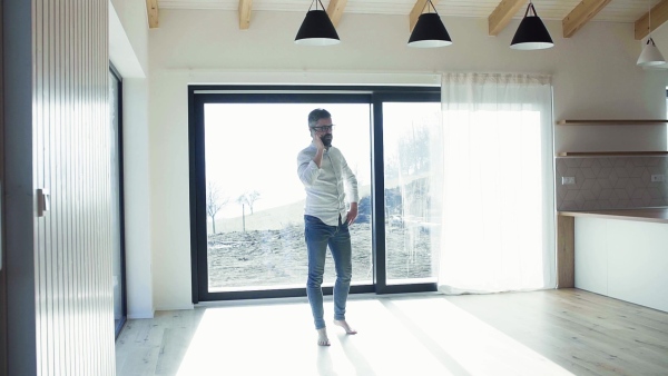 Mature man with smartphone in unfurnished house, moving in new home concept. Slow motion.