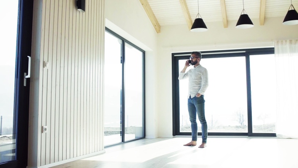 Mature man with smartphone in unfurnished house, moving in new home concept. Slow motion.