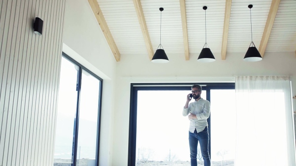 Mature man with smartphone in unfurnished house, moving in new home concept. Slow motion.