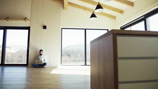 A mature man sitting on the floor in unfurnished new house, using laptop. A new home concept. Slow motion.