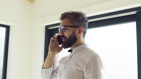 Serious mature man with smartphone in unfurnished house, moving in new home concept.