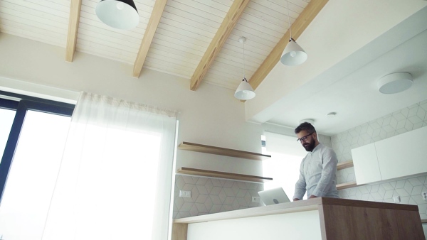 A mature man with laptop standing in kitchen in unfurnished new house. A new home concept. Slow motion.