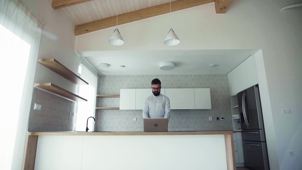 A mature man with laptop standing in kitchen in unfurnished new house. A new home concept. Slow motion.