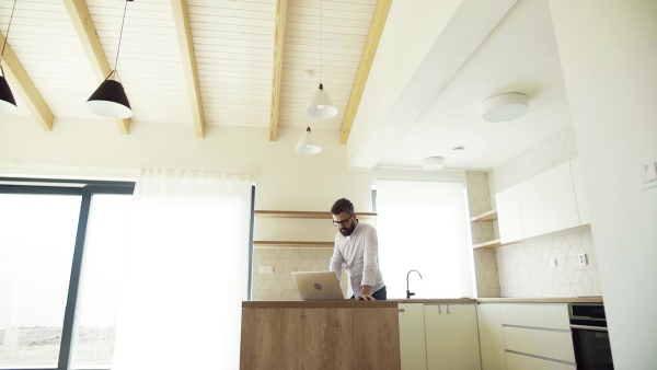 A mature man with laptop standing in kitchen in unfurnished new house. A new home concept. Slow motion.