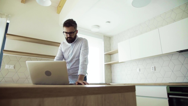 A mature man with laptop standing in kitchen in unfurnished new house. A new home concept. Slow motion.