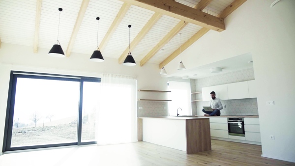 A mature man with laptop sitting on kitchen counter in new house. Moving in new home concept. Slow motion.