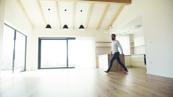 A mature man jumping in unfurnished house, moving in new home concept. Slow motion.