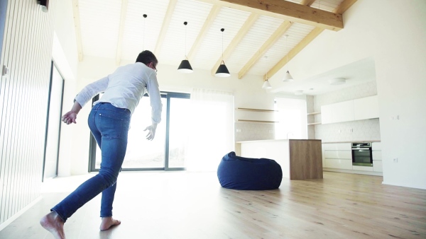 Cheerful mature man jumping into bean bag in unfurnished house, moving in new home concept. Slow motion.