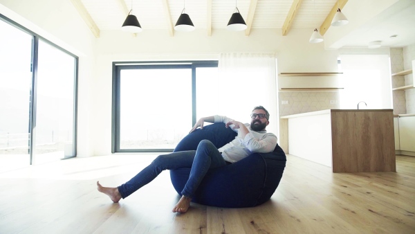 Cheerful mature man jumping into bean bag in unfurnished house, moving in new home concept. Slow motion.