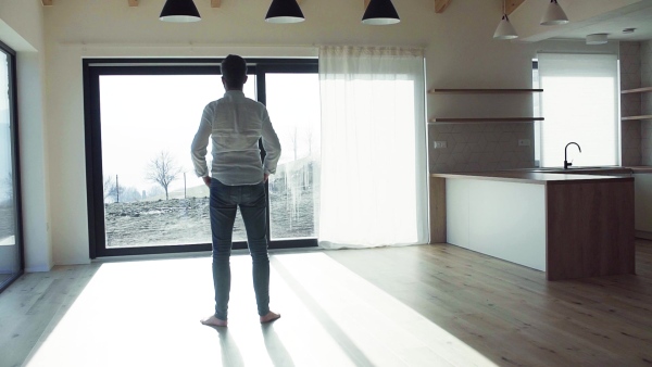 Rear view of mature man standing in unfurnished house, moving in new home concept. Slow motion.