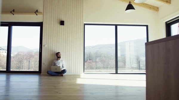 A mature man sitting on the floor in unfurnished new house, using laptop. A new home concept. Copy space.