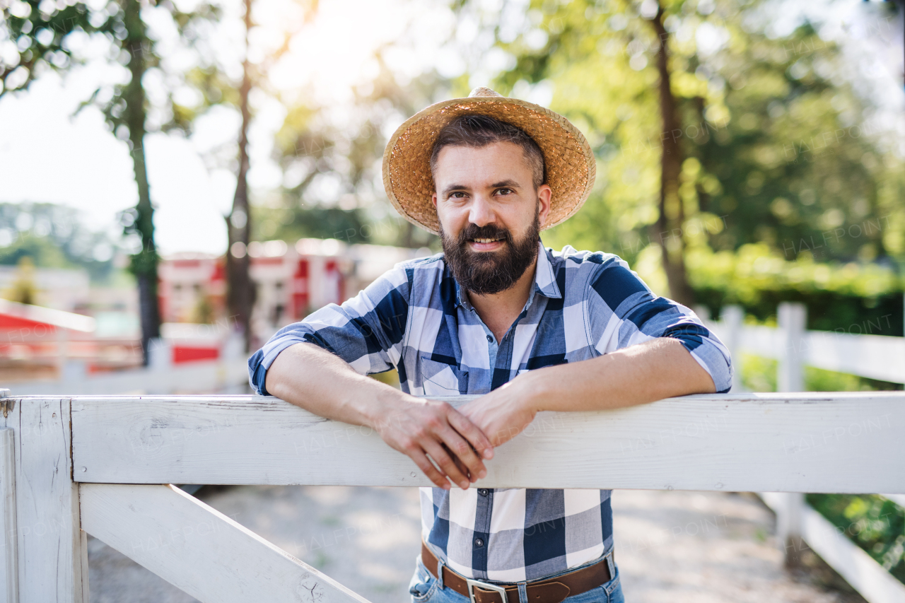 A portrait of mature man farmer with hat standing outdoors on family farm.