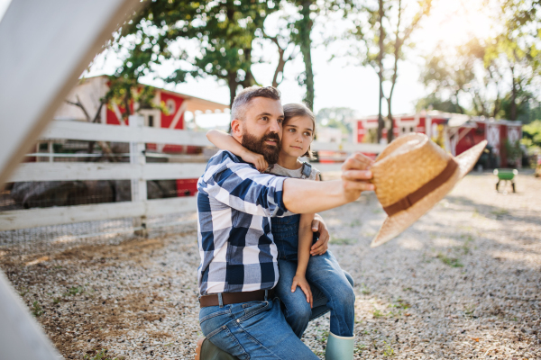 A mature father with small daughter outdoors on family farm, talking.