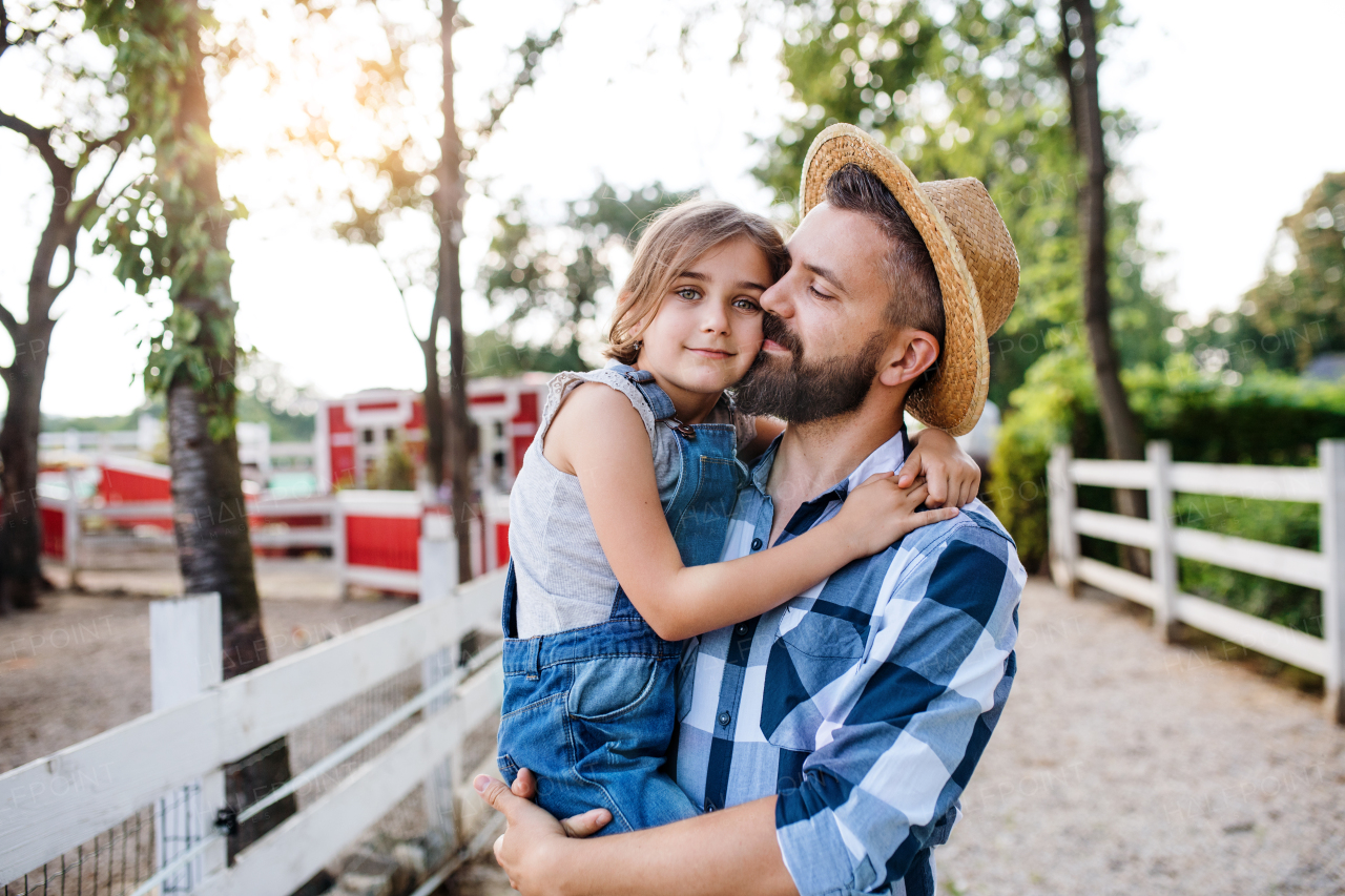 A mature father with small daughter walking outdoors on family farm.