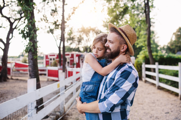 A mature father with small daughter walking outdoors on family farm.