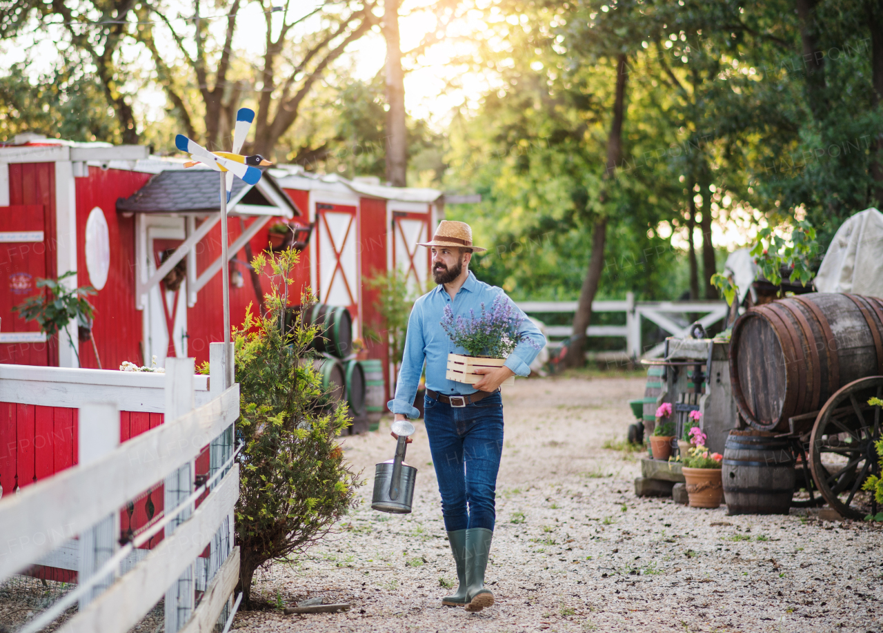 Front view of farmer walking outdoors on small family farm, carrying watering can.