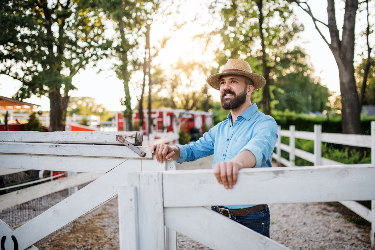 A portrait of mature farmer walking outdoors on family farm, opening gate.