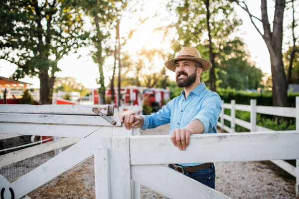 A portrait of mature farmer walking outdoors on family farm, opening gate.