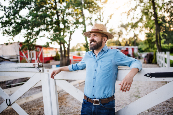 A portrait of farmer standing outdoors on family farm, standing by wooden gate.