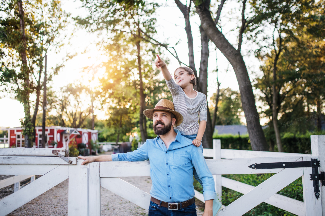 A portrait of father with small daughter outdoors on family farm, looking at camera.