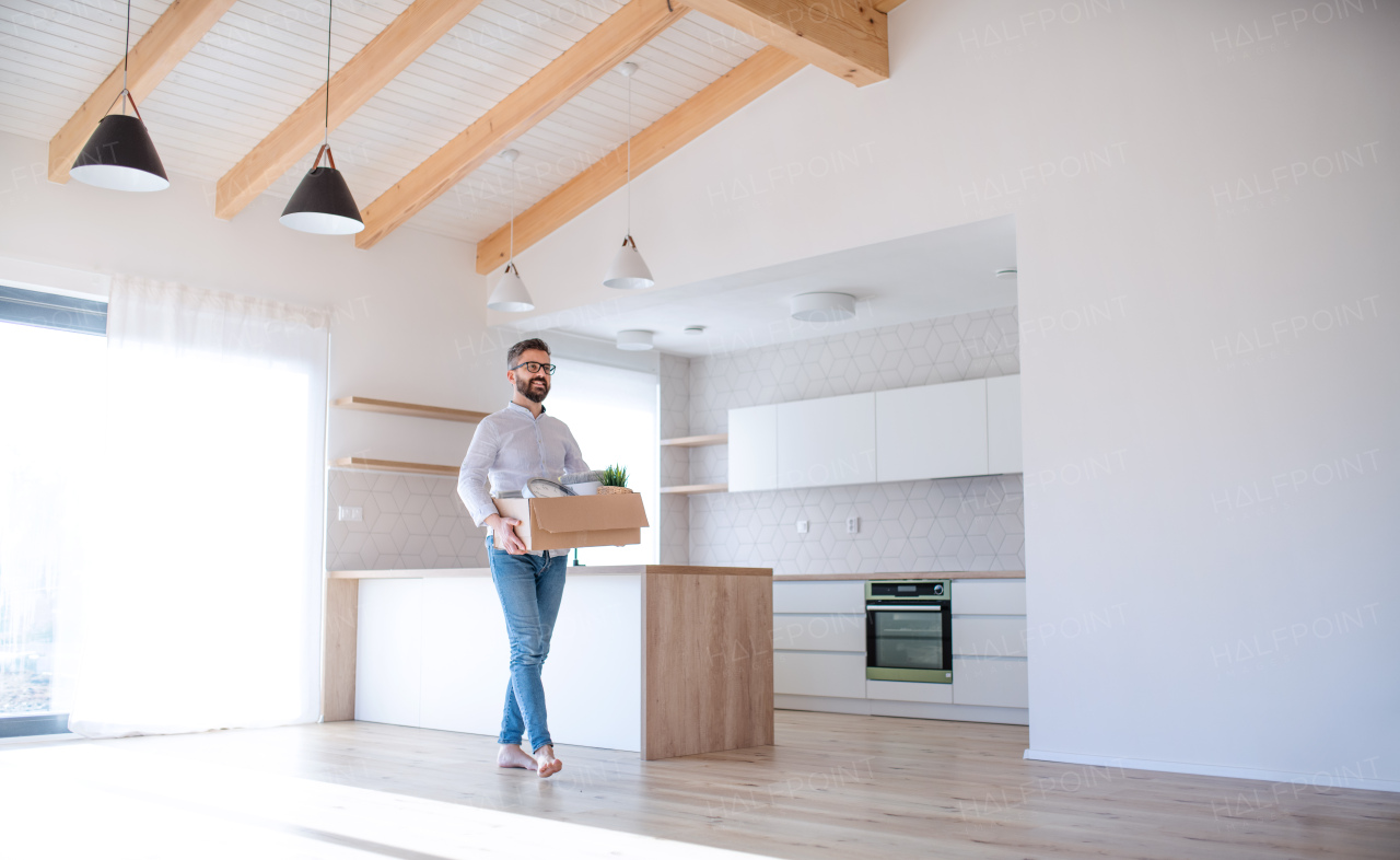 A mature man walking in unfurnished house, holding a box. A moving in new home concept.