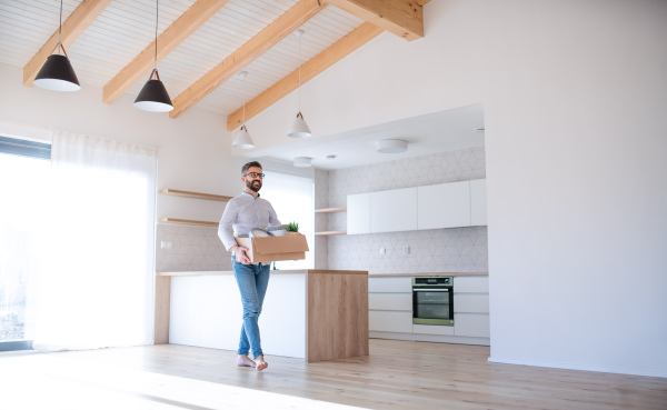 A mature man walking in unfurnished house, holding a box. A moving in new home concept.