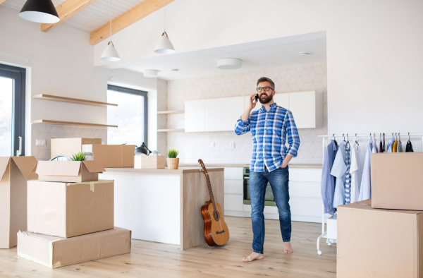 A mature man with boxes moving in new house, using smartphone.