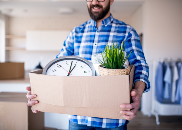 A midsection of mature man with box moving in new unfurnished house.