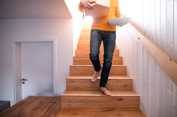 Unrecognizable man with boxes moving in new unfurnished house, walking down the stairs.