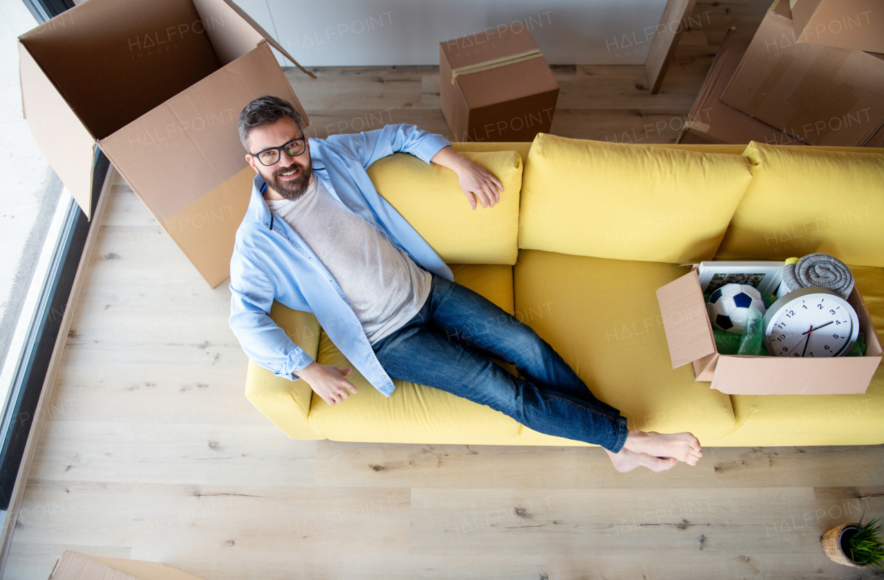 Top view of mature man with boxes moving in new house, lying and relaxing on sofa.