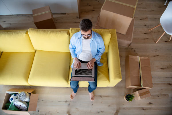 Top view of mature man sitting on sofa in unfurnished house, using laptop. A moving in new home concept.