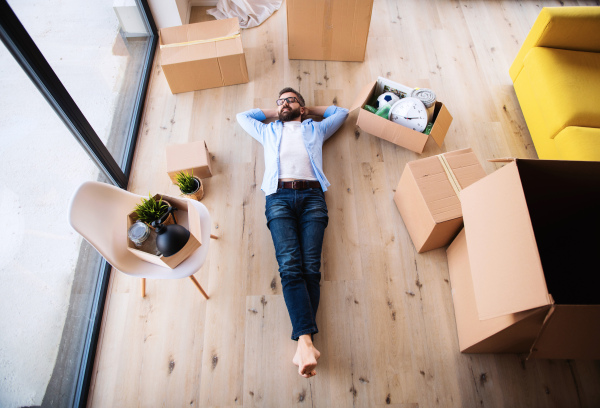 A top view of mature man with boxes moving in new house, relaxing.