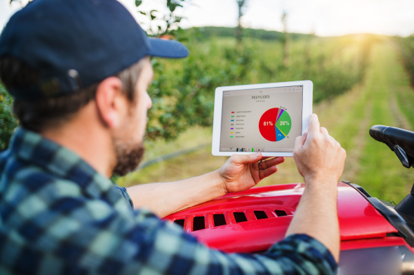 A mature farmer with tablet standing by mini tractor outdoors in orchard, checking pesticides statistics.